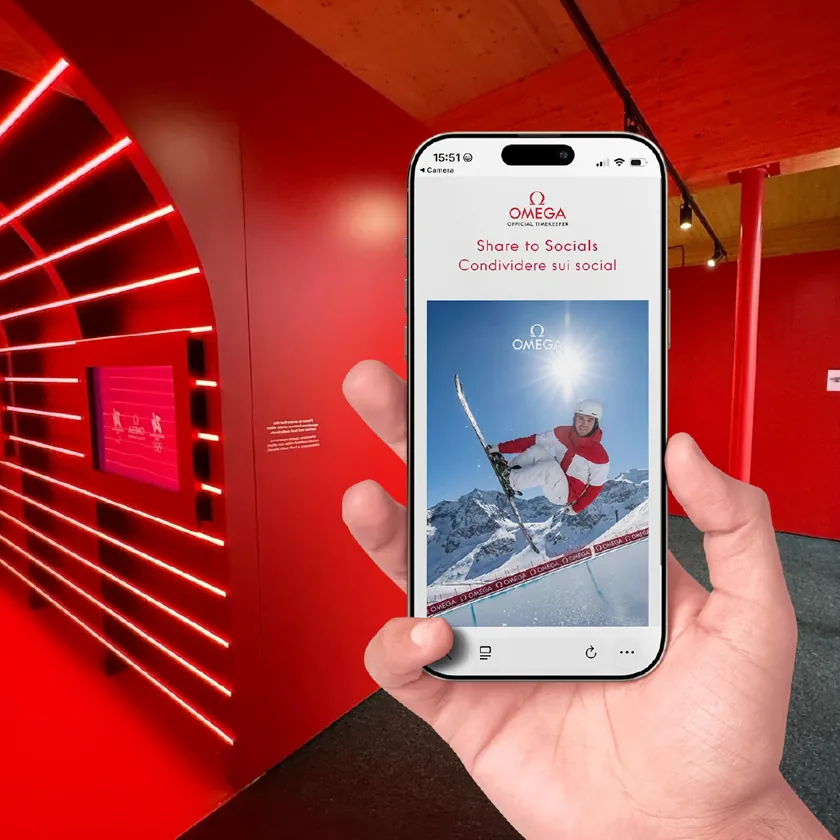 Hand holding a phone showing a branded photo of a snowboarder mid-jump, in a red-lit exhibition space
